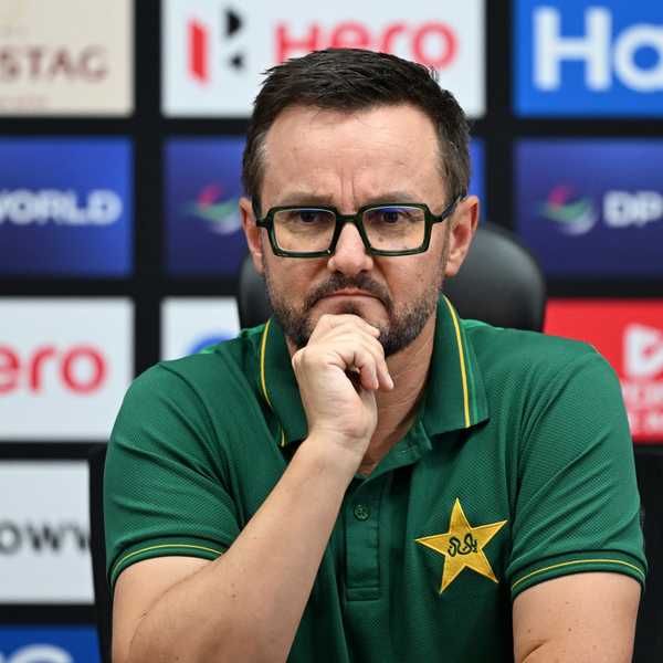 Man in a green shirt with star logo, sitting pensively at a press conference.