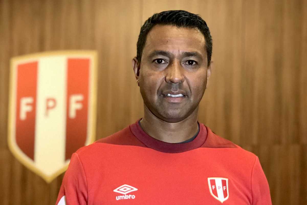 Man in a red Peru team jacket stands before an FPF logo on a wood-paneled wall.