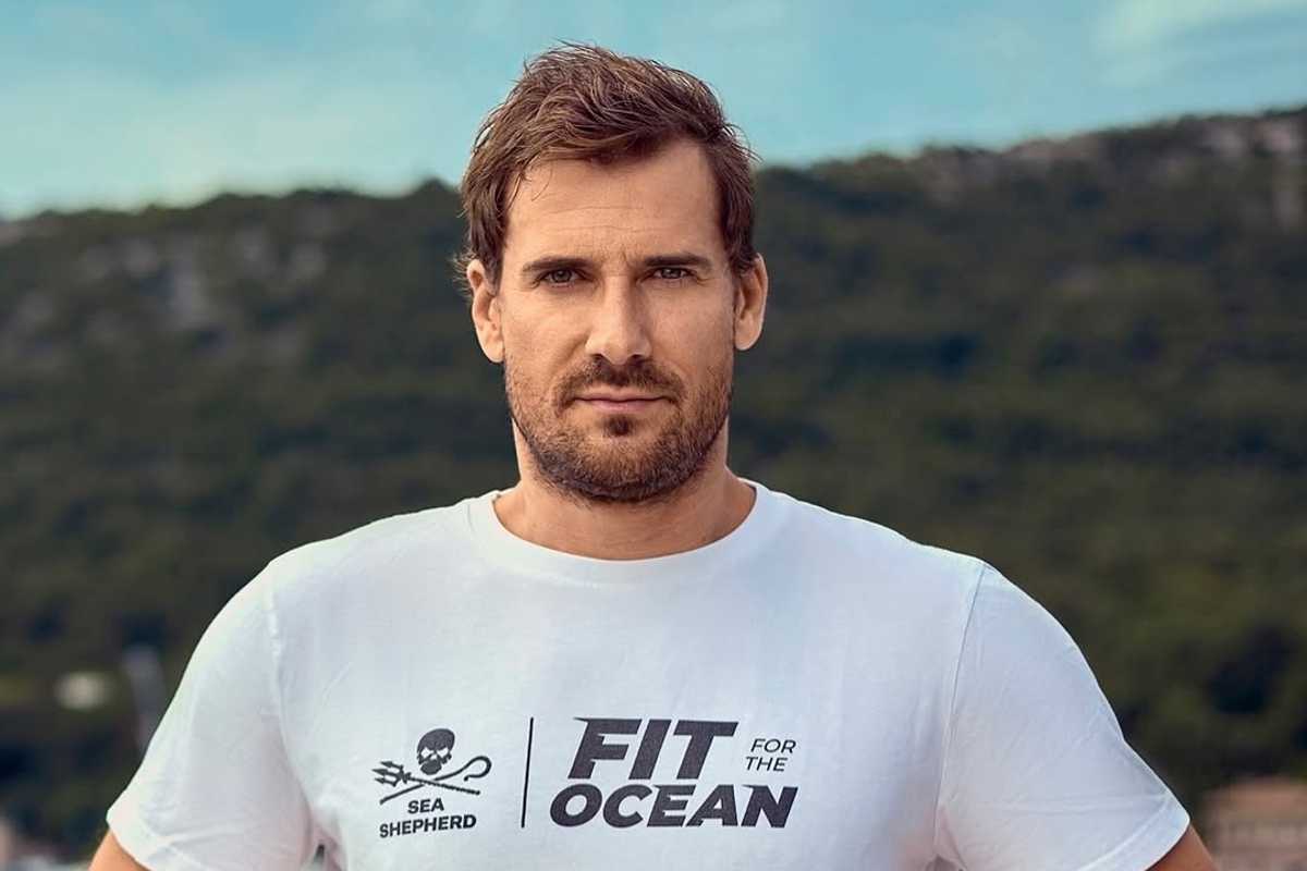 Man in "Fit for the Ocean" shirt, outdoors with hills in the background.