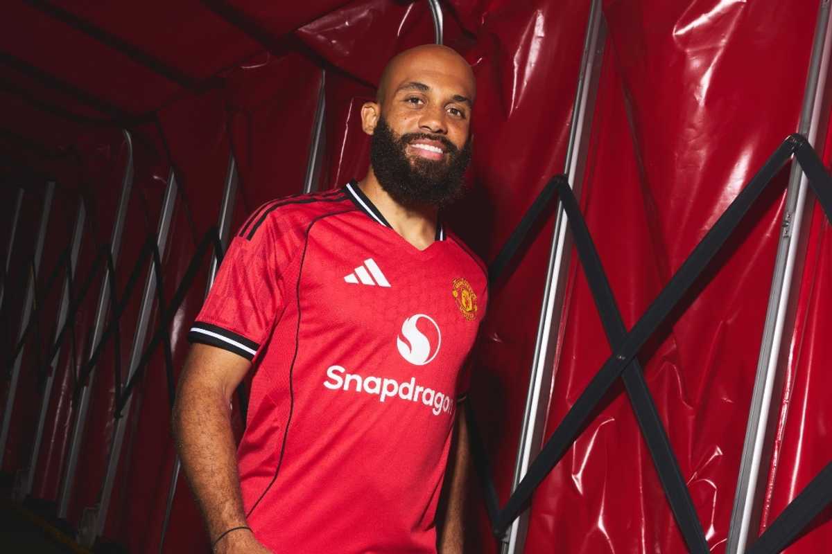 Man in red Manchester United jersey standing in a red tunnel, smiling.