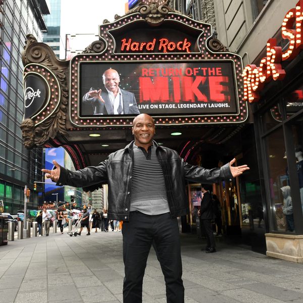 Man standing with arms outstretched in front of Hard Rock Cafe marquee in a city.