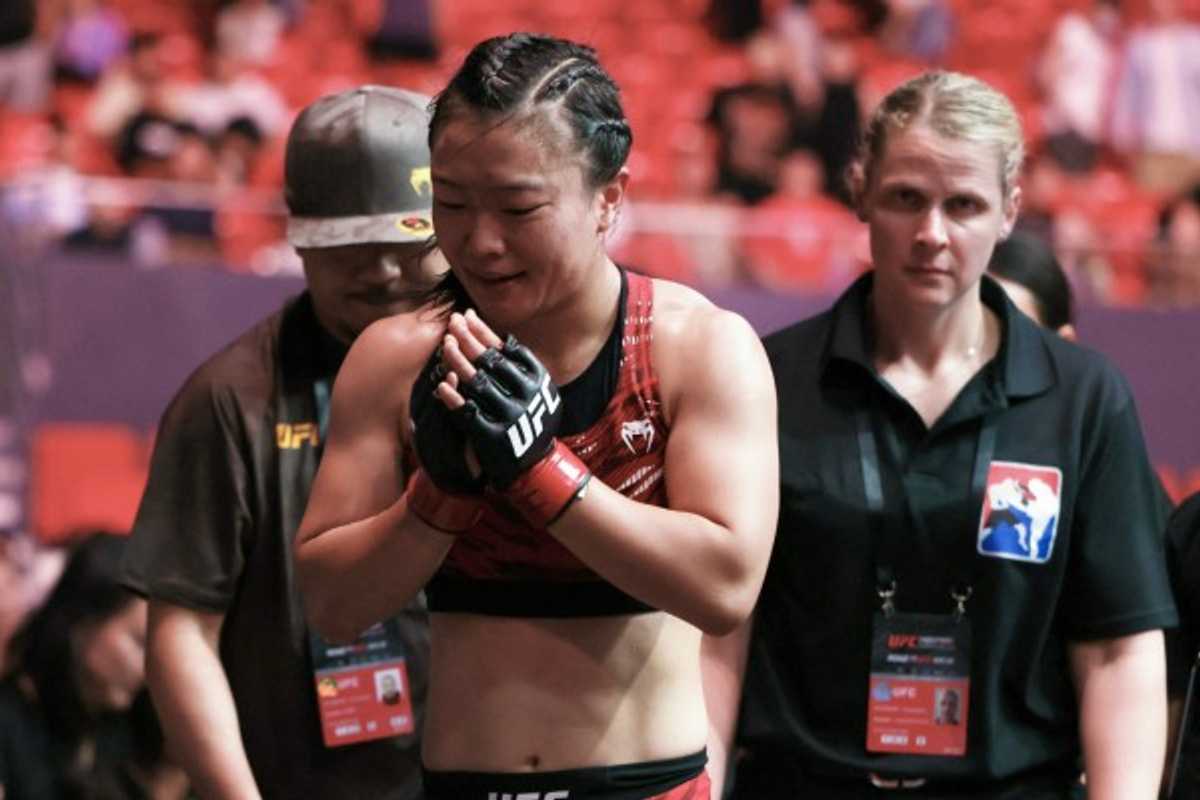 MMA fighter in red gear entering the arena, flanked by team and officials.