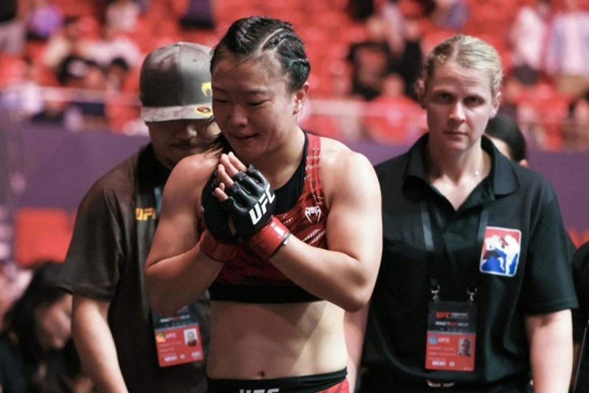 MMA fighter in red gear entering the arena, flanked by team and officials.