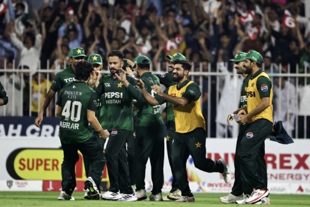 Pakistani cricket team celebrates a wicket on the field with cheering crowd in the background.