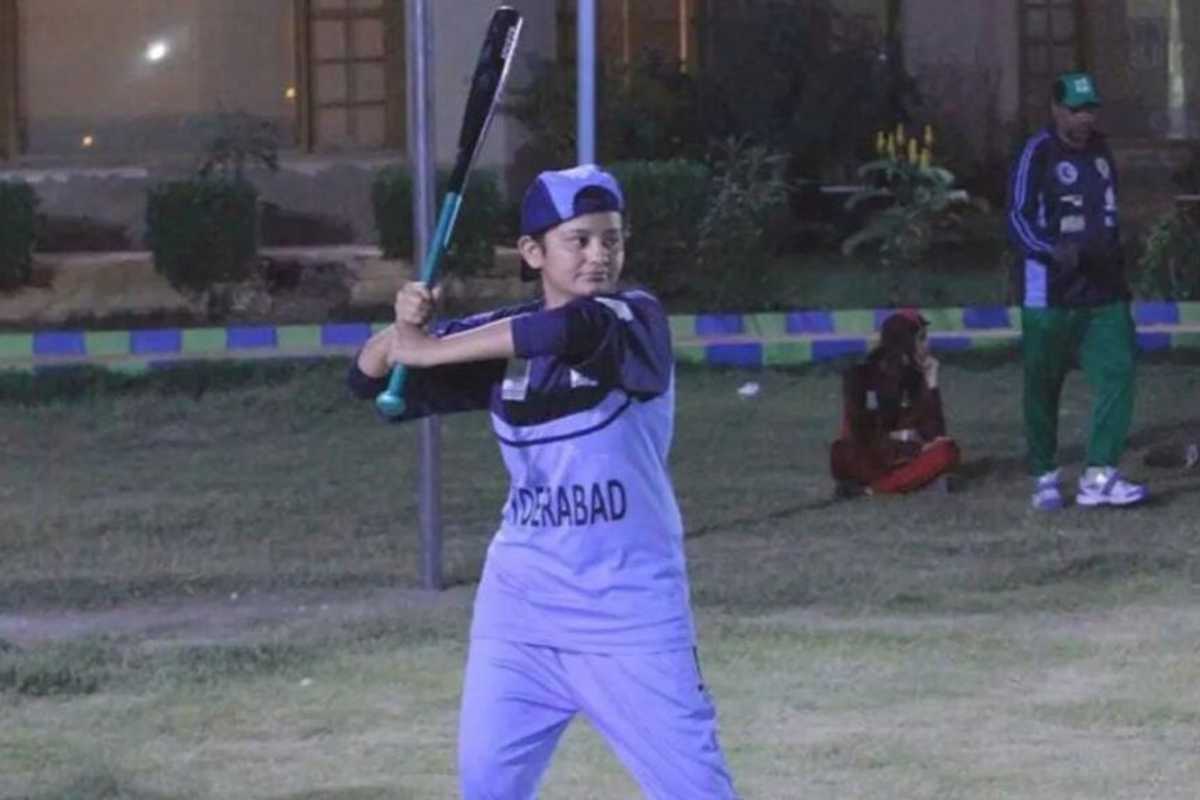 Person in a blue uniform batting in a baseball game on a grassy field at night.