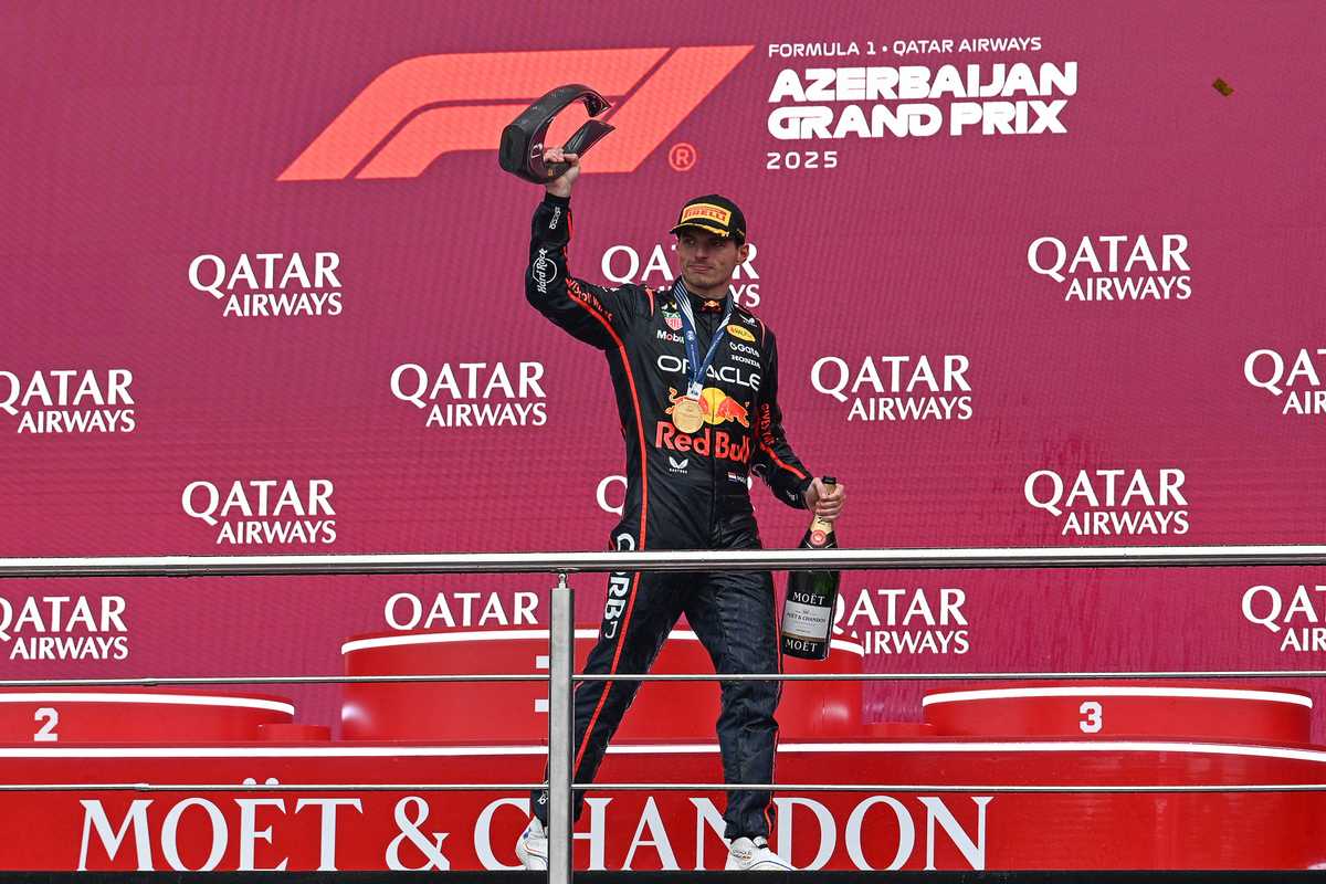 Race car driver celebrates on podium at Azerbaijan Grand Prix with trophy and champagne.