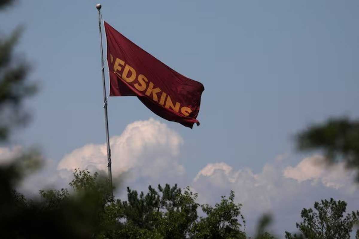 Red flag with "EDSKINS" flying above treetops against a cloudy sky.