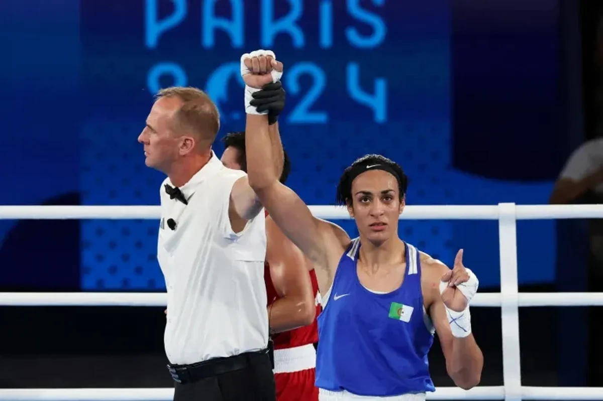 Referee raises the arm of a victorious female boxer in a blue jersey at Paris 2024.