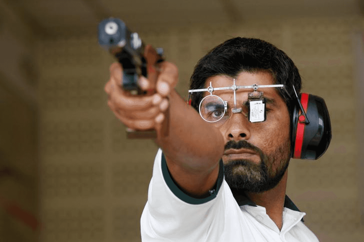 Shooter aiming a pistol with focus glasses and earmuffs.