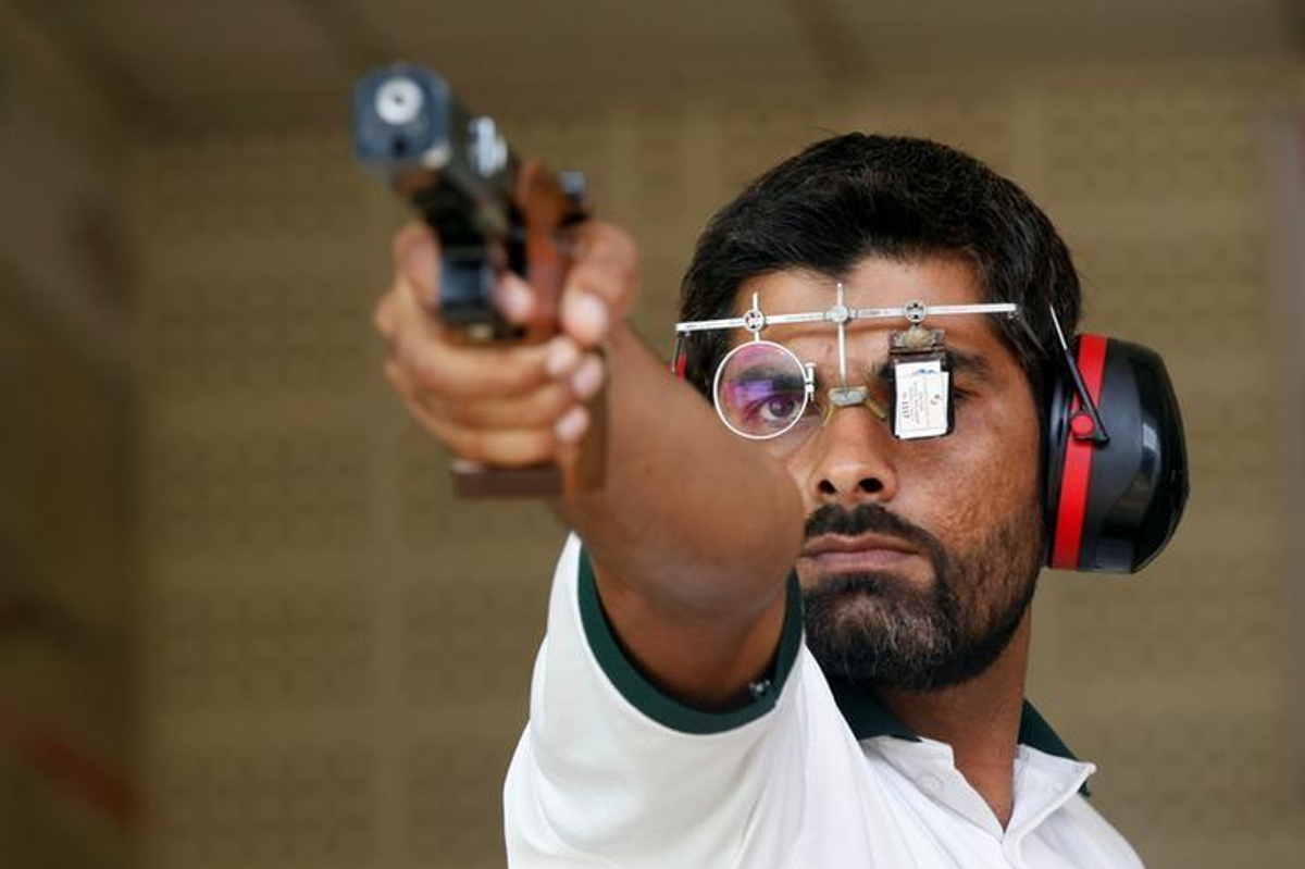 Shooter aiming a pistol with focus glasses and earmuffs.