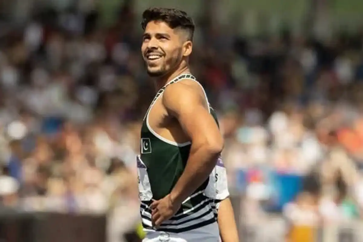 Smiling athlete in track uniform looks back at a stadium crowd.
