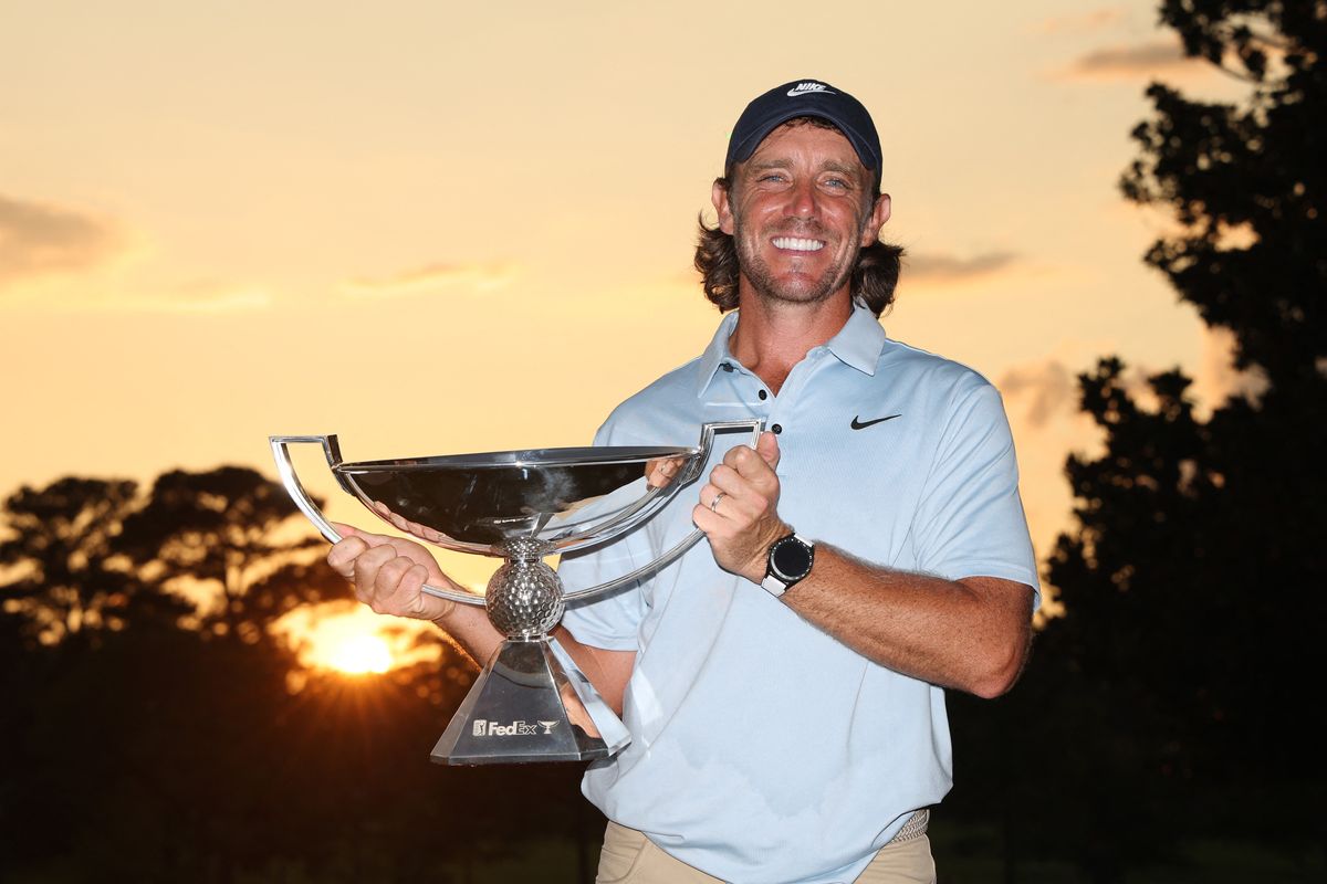 Smiling man holding a golf trophy at sunset.