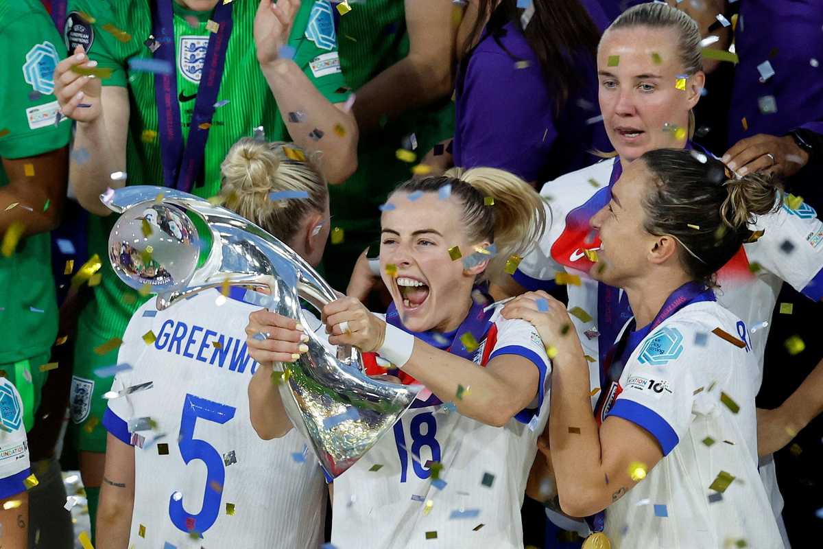 Soccer player celebrating with a trophy amidst confetti and teammates in white jerseys.