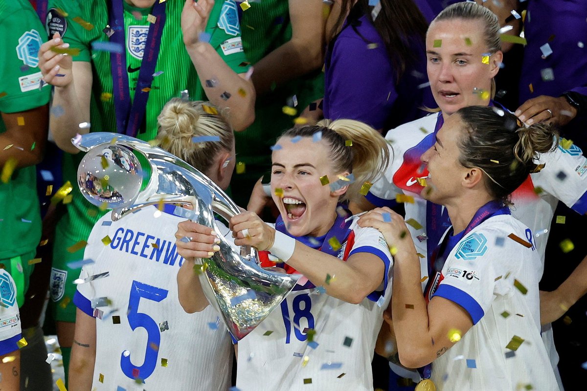 Soccer player celebrating with a trophy amidst confetti and teammates in white jerseys.