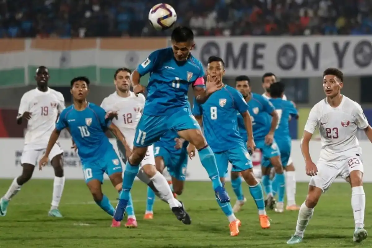 Soccer player heads ball during intense match; team in blue and team in white compete.