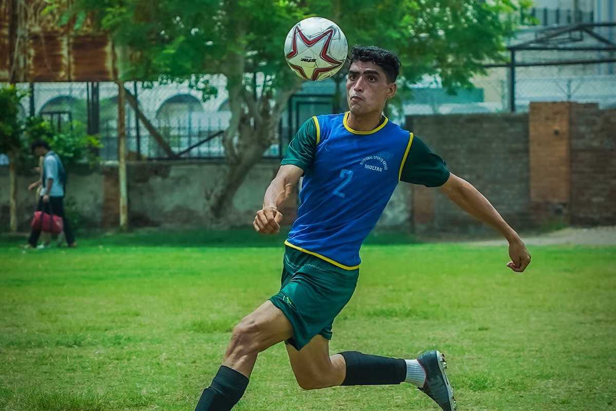 Soccer player in green jersey controlling the ball mid-air on a grassy field.