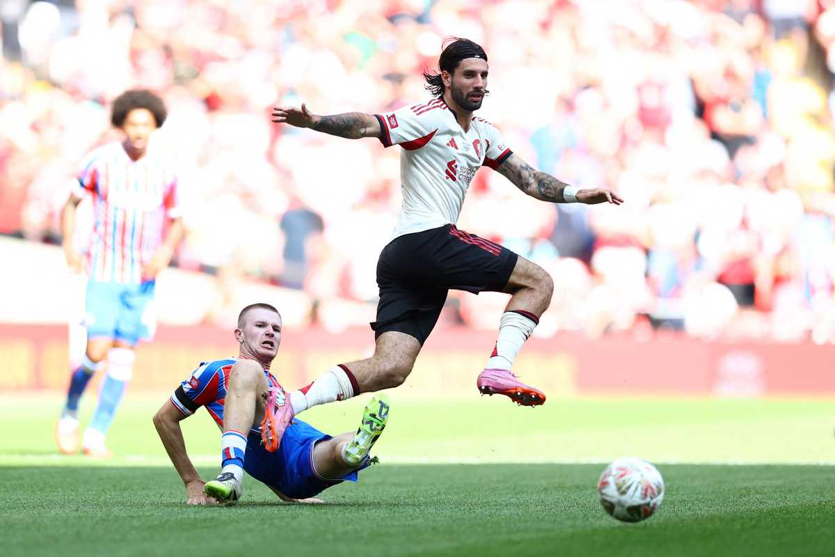 Soccer player jumps over a sliding opponent during a match, with a ball nearby.
