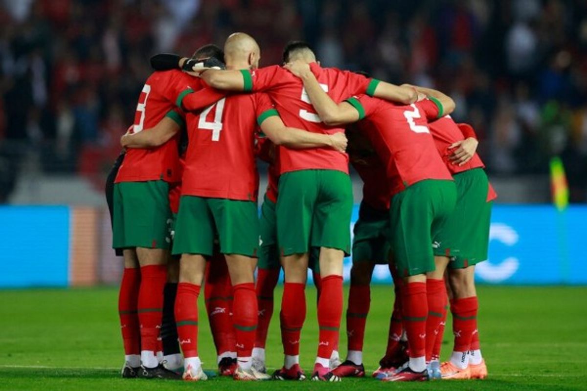 Soccer players in red jerseys huddle on the field before a match.