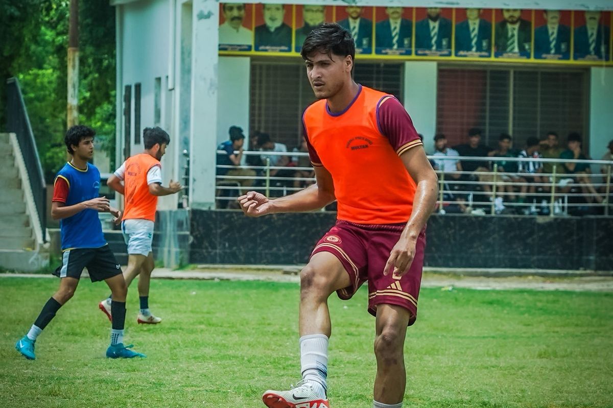 Soccer players practicing on a field, one in an orange vest, others in blue and white.