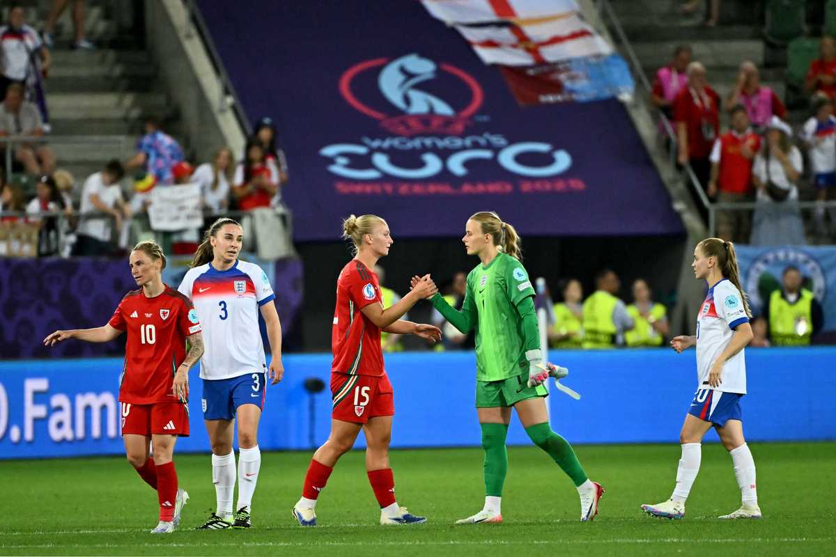 Soccer players shake hands on the field at UEFA Women's Euro, large banner in background.