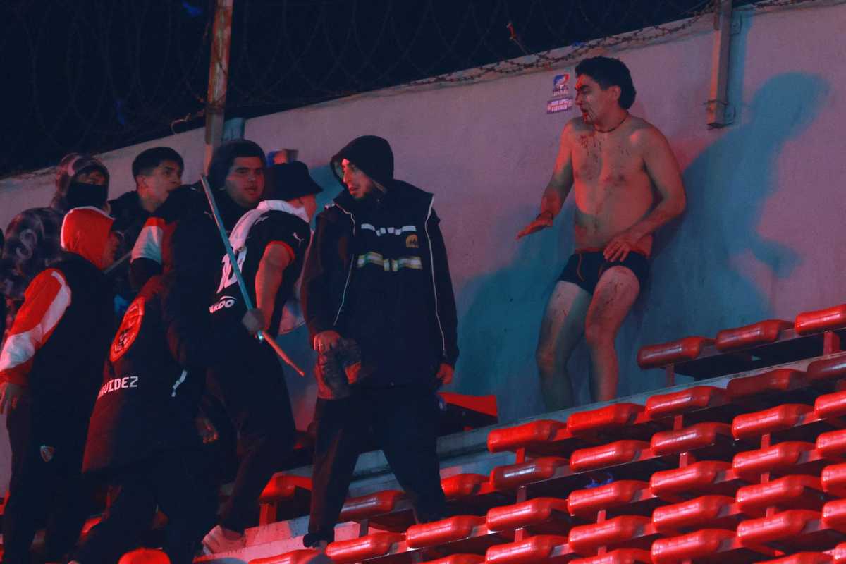 Stadium altercation with a shirtless man and people wearing jackets holding sticks.