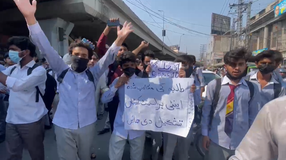Students protest on a street, holding a sign and wearing uniforms.