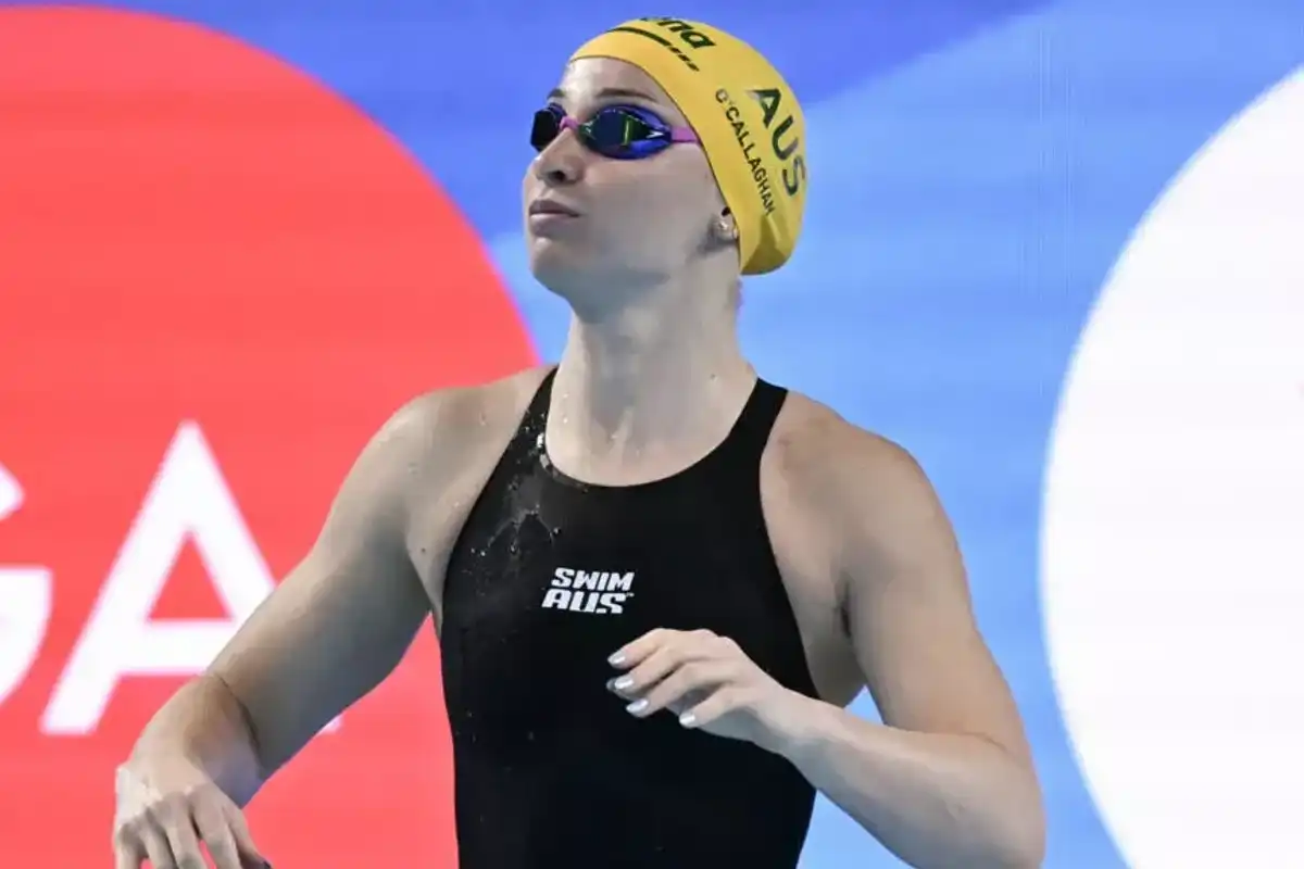 Swimmer in yellow cap and black suit looks up poolside.