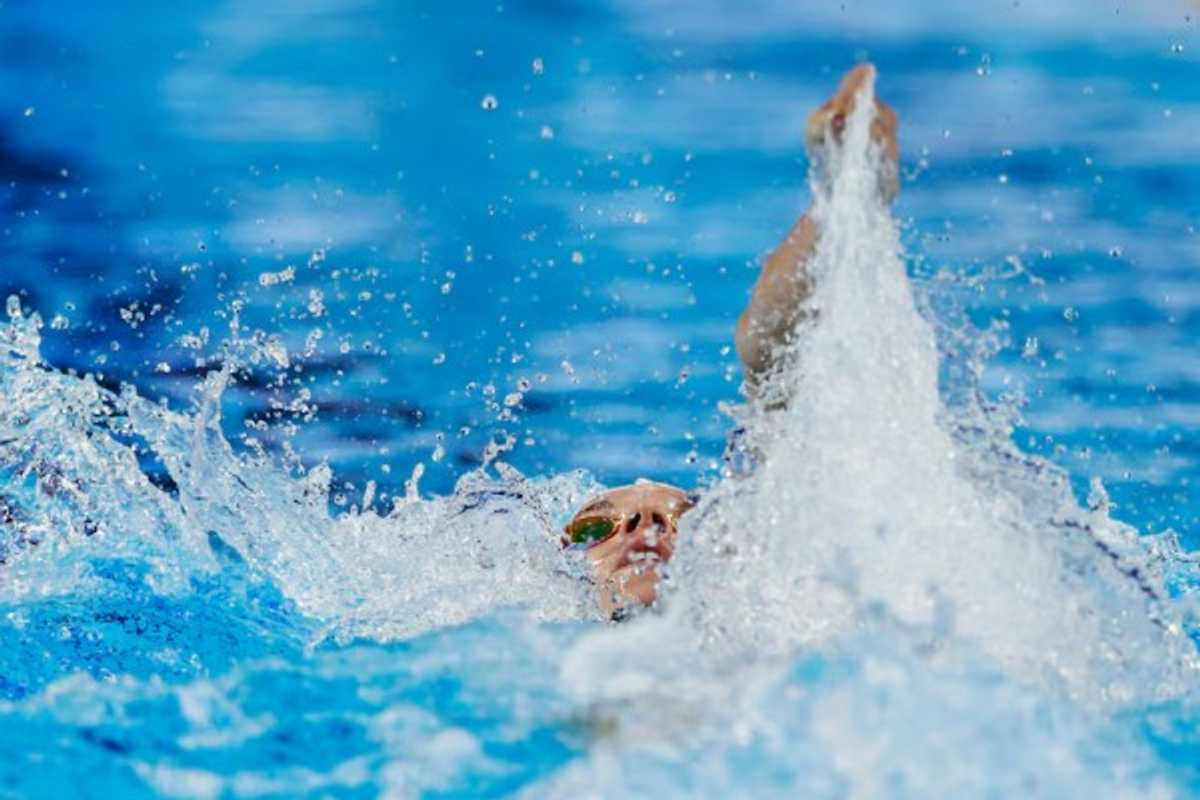 Swimmer performing backstroke with water splashing around in a pool.