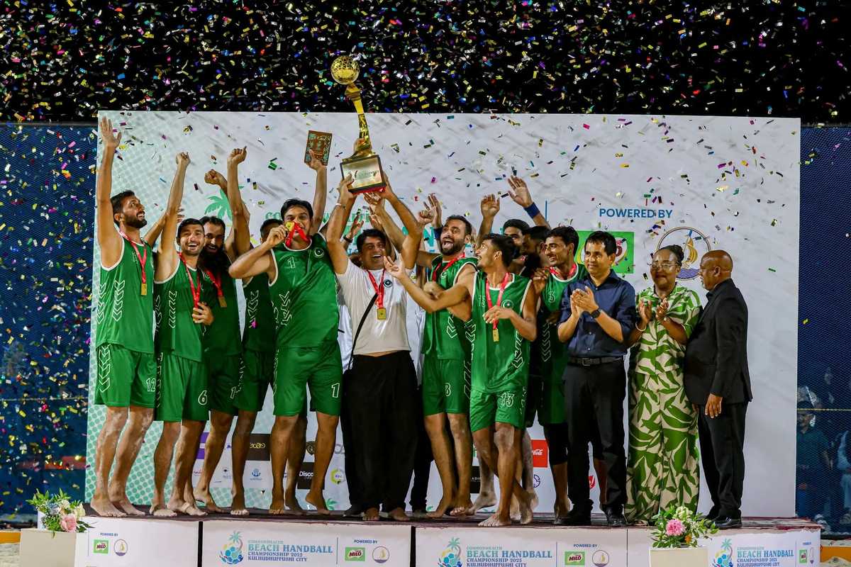 Team celebrates victory, lifting trophy amid confetti on stage.