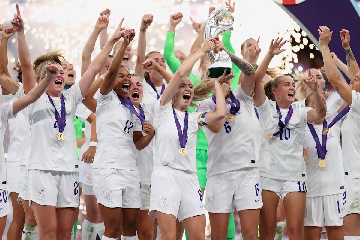Team celebrating with a trophy, wearing white jerseys and gold medals, surrounded by confetti.