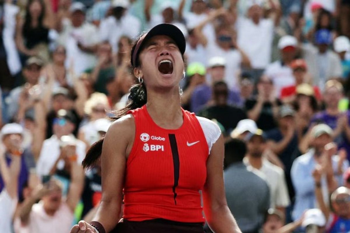 Tennis player celebrates victoriously on the court, crowd cheering in the background.
