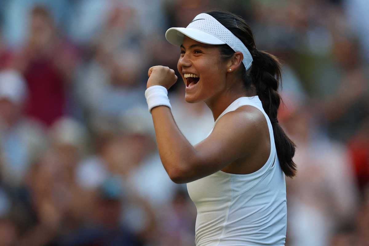 Tennis player celebrates with a fist pump on court, wearing white attire and visor.