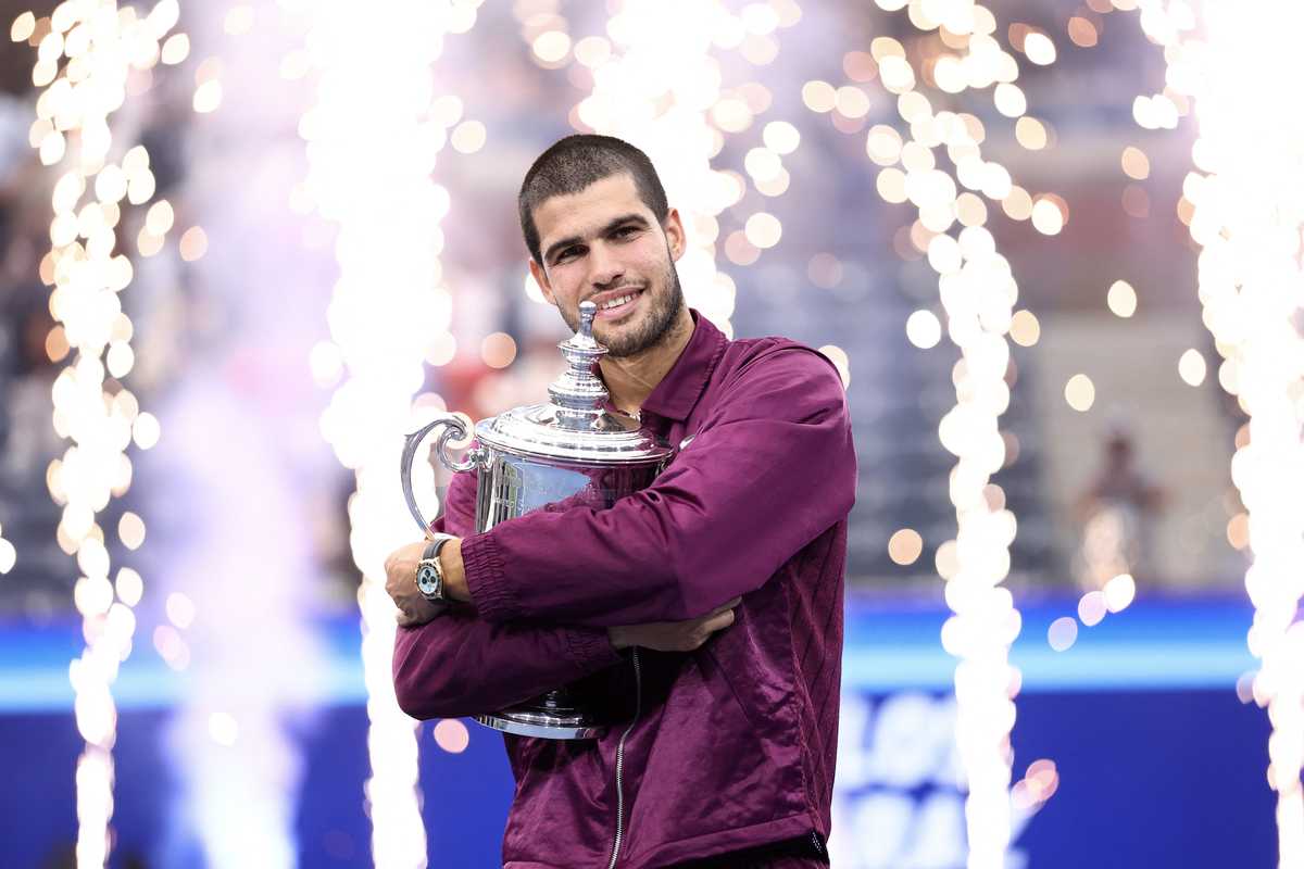 Tennis player holding trophy with fireworks in background.