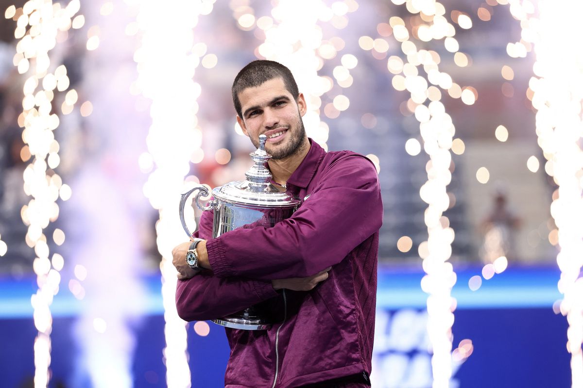 Tennis player holding trophy with fireworks in background.