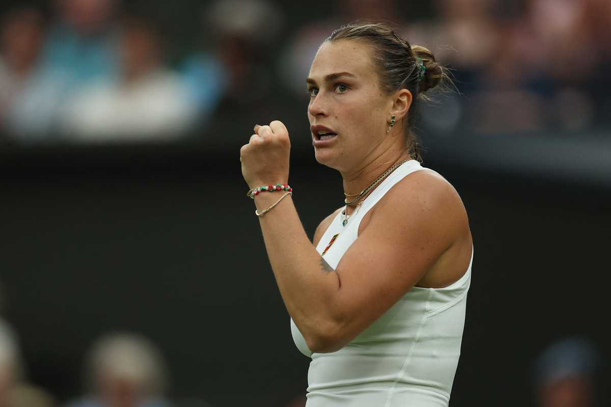 Tennis player in action, fist clenched, wearing white outfit, focused expression.
