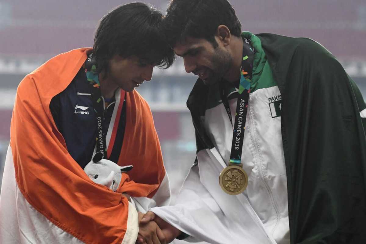 Two athletes exchange a handshake, wearing medals and draped in their national flags.