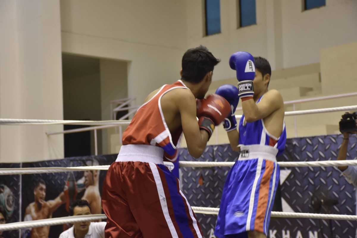 Two boxers in red and blue gear spar in a boxing ring.