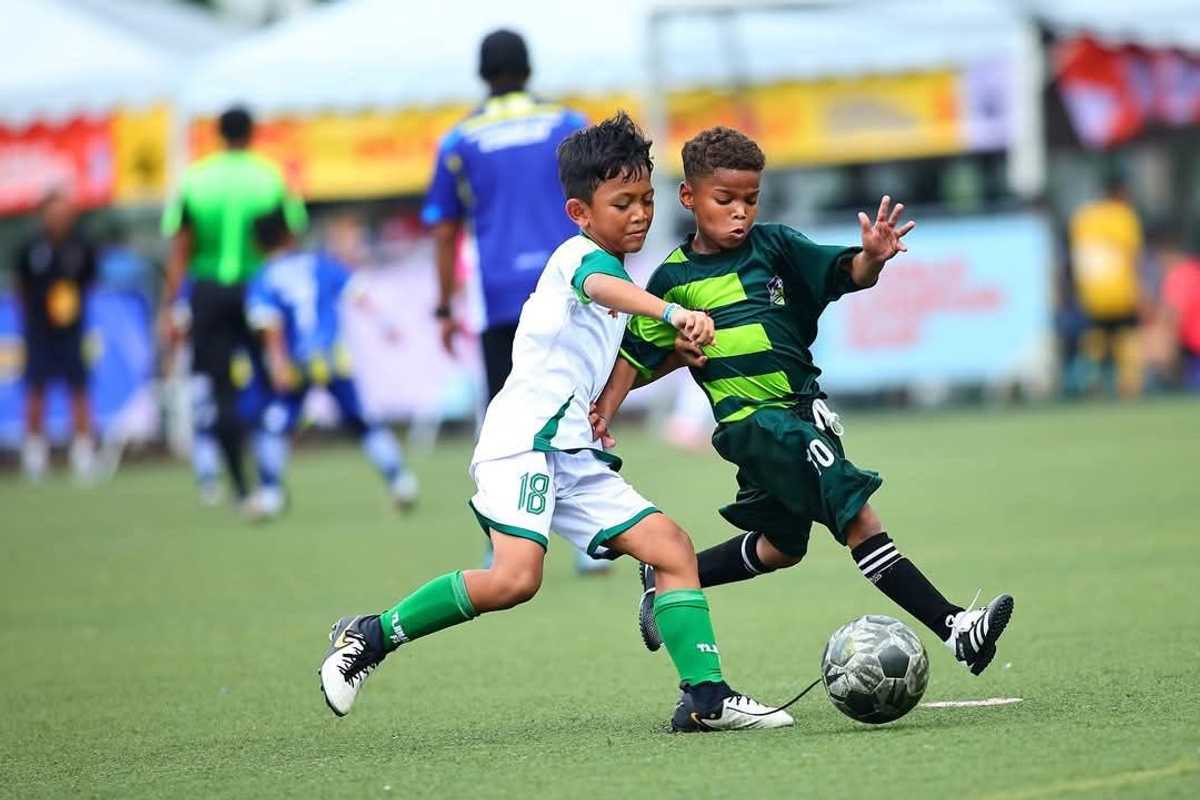 Two boys in green uniforms playing soccer, competing for the ball.