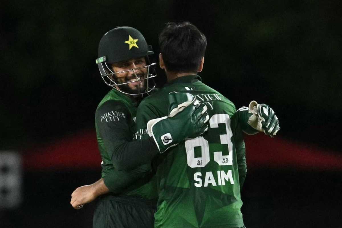 Two cricketers in green jerseys celebrate with a hug on the field.