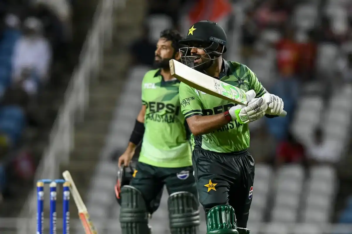 Two cricketers in green uniforms during a match, one gesturing with his bat.