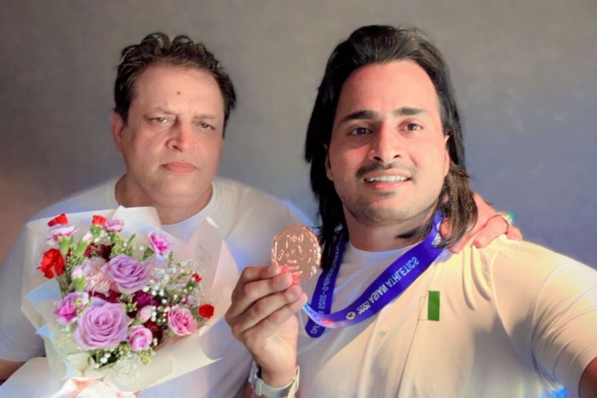 Two men holding a bouquet and a medal, smiling at the camera.