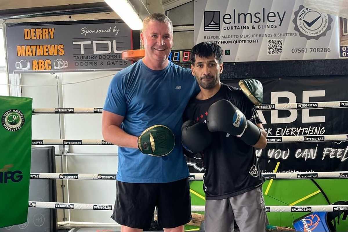 Two men in a boxing gym, wearing gloves, posing for a photo.