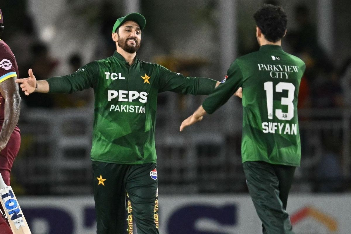 Two Pakistani cricketers in green uniforms celebrating on the field.
