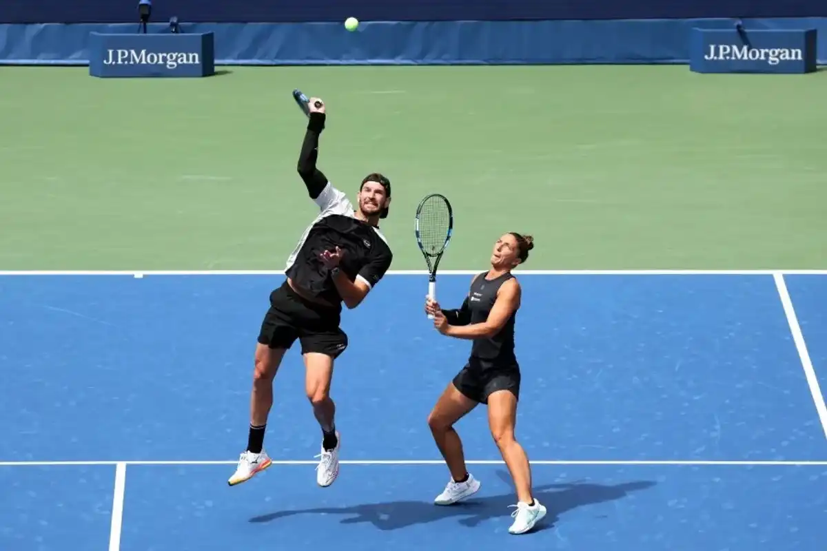 Two tennis players on a blue court, with one jumping to hit the ball.