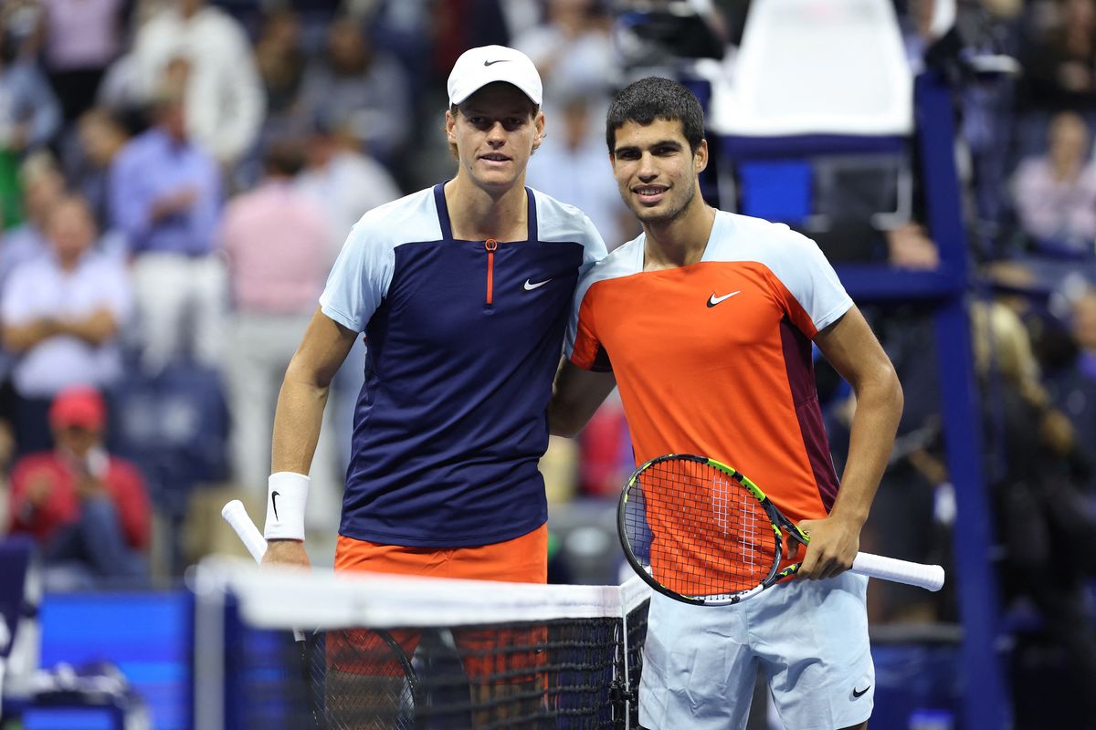 Two tennis players pose at the net on a court, surrounded by a cheering crowd.