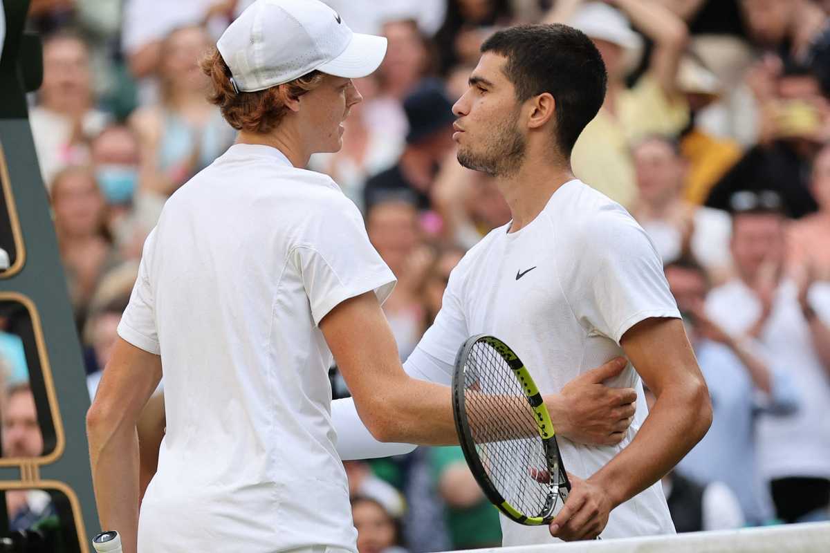 Two tennis players shake hands at the net after a match in a crowded stadium.