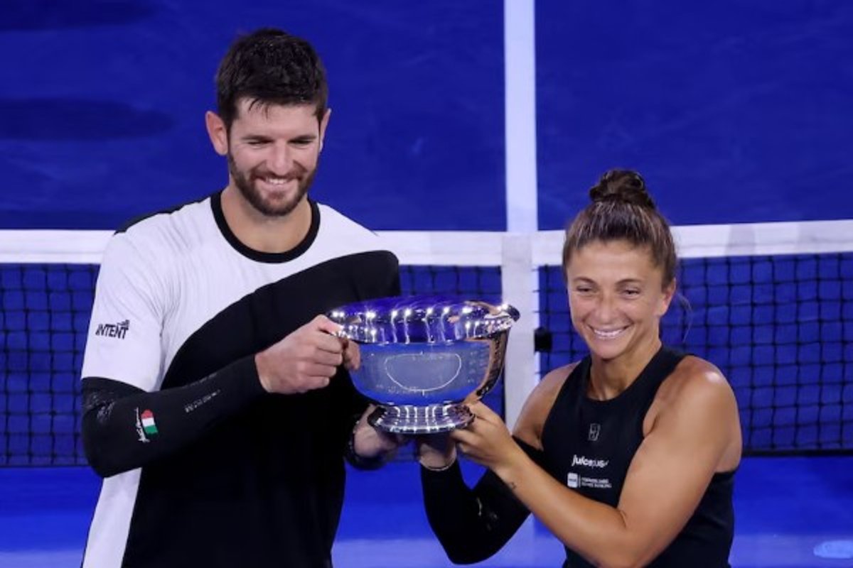 Two tennis players smiling, holding a silver trophy on a blue court.