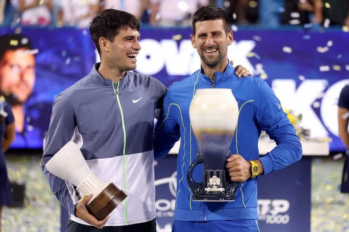 Two tennis players smiling, holding trophies on a confetti-filled court.