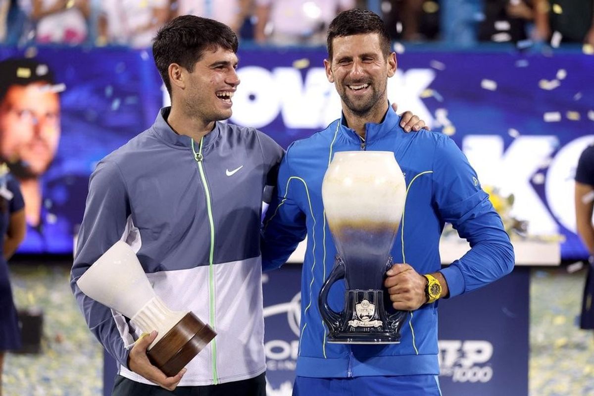 Two tennis players smiling, holding trophies on a confetti-filled court.